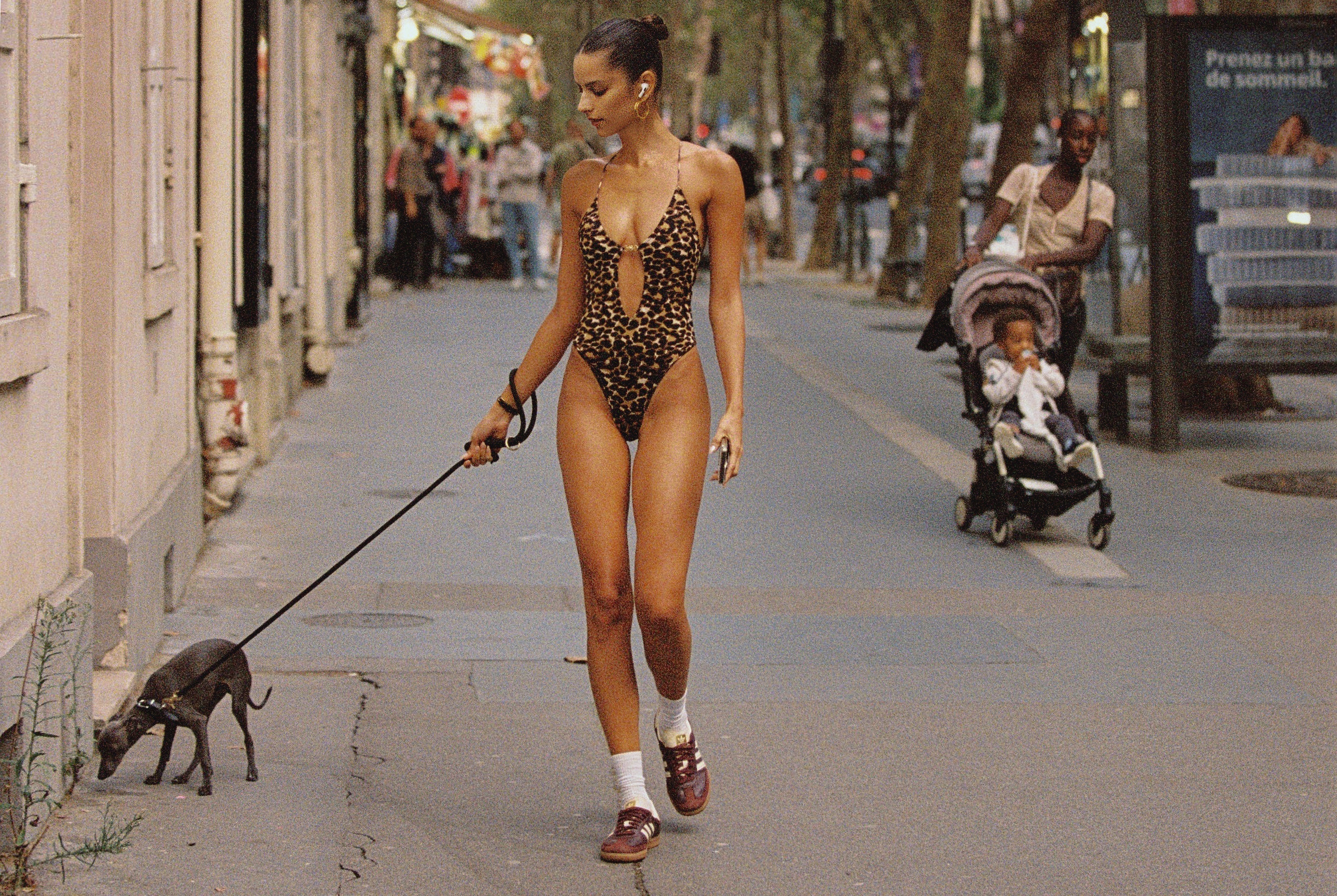 Model in the streets of paris walking a dog in a one piece leopard swimsuit with small stomach cut out and gold hardware